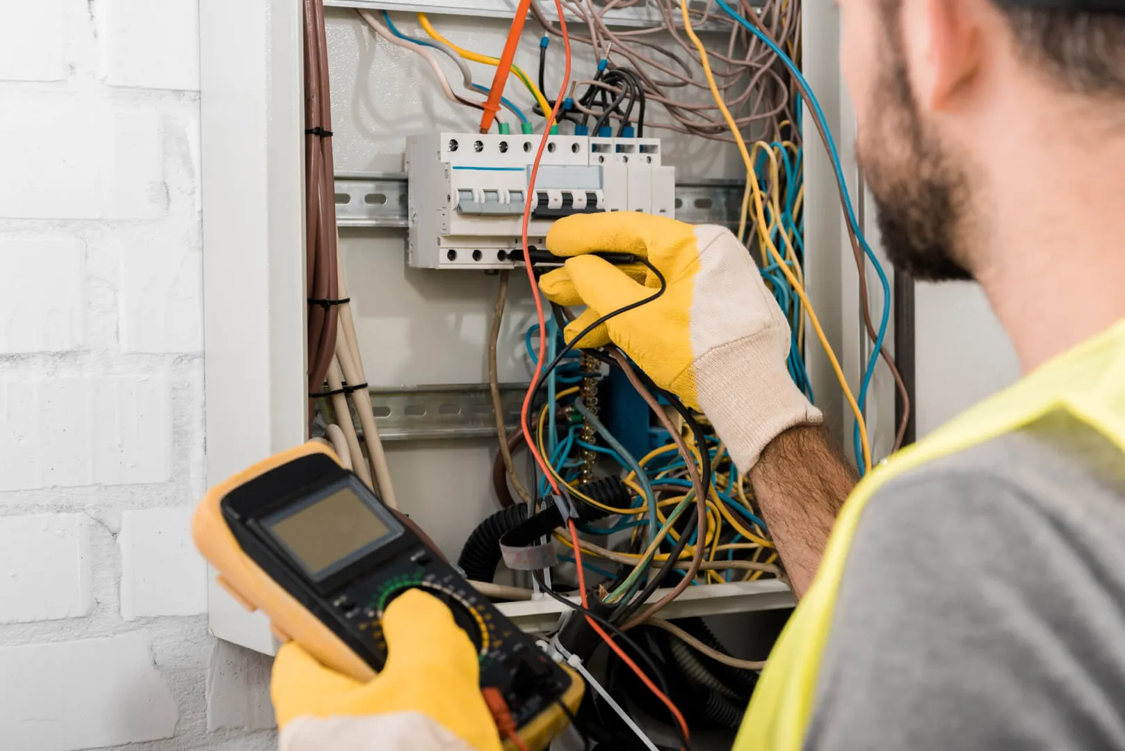 Electrician troubleshooting electrical panel with multimeter.